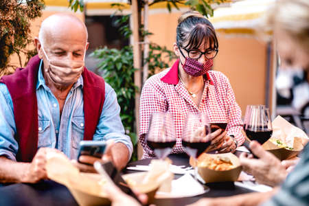 Senior people using mobile smart phone with face mask covered - Retired adults worried while watching news on smartphone - New normal lifestyle concept at restaurant wine bar - Vivid contrast filterの写真素材