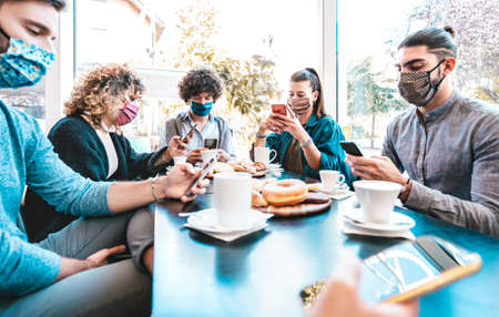 Worried business employees using mobile smart phones at coffee break - New normal lifestyle concept with people wearing face mask on contact tracing app - Bright filter with focus on middle frameの写真素材