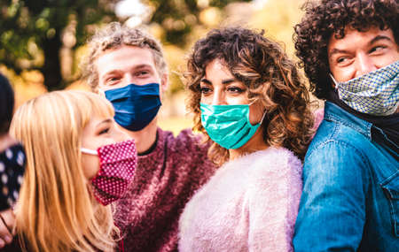Happy multiracial friends having fun together wearing face masks - New normal friendship concept with young people sharing free time outside at park - Warm filter with focus on left woman eyesの写真素材