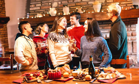 Happy people group celebrating Christmas party at dinner supper fest - Winter holiday concept with young friends sharing time and having fun eating together - Warm filter with focus on central womanの写真素材