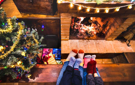 Mother father and kids sitting at cozy fireplace on winter time - Lovely family resting together on woolen socks at home fire place - Christmas holidays concept on comfy house venue - Warm filterの写真素材