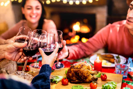 People toasting red wine having fun at Christmas dinner reunion - Holiday celebration concept with happy family sharing winter time together at home supper feast - Warm filter with focus on glassesの写真素材