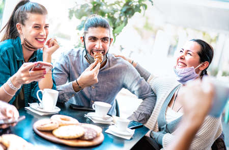 Friends having fun eating croissants at coffee house - Young people laughing together at restaurant cafeteria - New normal lifestyle concept with happy men and women at cafe bar - Bright azure filterの写真素材