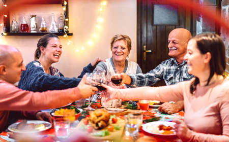 People toasting red wine and having fun at winter holidays reunion - Dinner celebration concept with happy adult friends sharing time together at home party - Warm filter with focus on central womanの写真素材