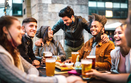 Young people drinking beer with open face mask - New normal lifestyle concept with milenial having fun together talking on happy hour at outside brewery bar - Warm filter with focus on central peopleの写真素材