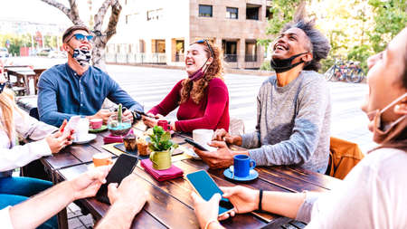 People having fun drinking latte outside at coffeehouse - Young friends talking together at restaurant cafeteria - New normal lifestyle concept with happy guys and girls at cafe bar - Bright filterの写真素材