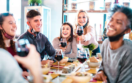 People toasting red wine at fashion restaurant bar with open face mask - New normal lifestyle concept with happy friends having fun together on bright filter - Focus on middle frame brunette womanの写真素材