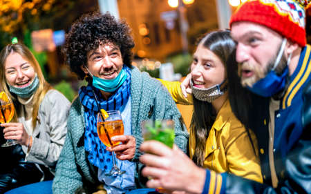 Friends drinking spritz and mojito at cocktail bar wearing open face mask - New normal lifestyle concept with happy people having fun together toasting drinks at outdoor restaurant - Focus on left guyの写真素材