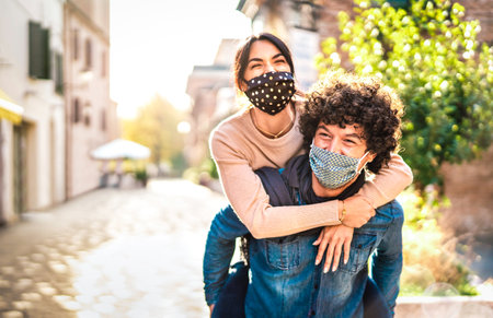 Happy couple of lovers enjoying time outdoor at Valentines day - Handsome guy with nice girl on piggy back moment - New normal love concept with boyfriend and girlfriend together on warm vivid filterの写真素材