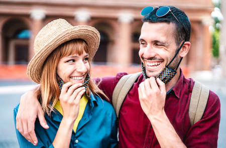 Happy travel couple smiling with open face mask - New normal lifestyle concept with young people on positive mood after lockdown reopening - Bright vivid contrast filter with focus on woman eyesの写真素材