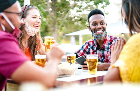 Multicultural people drinking beer with open face masks - New normal gathering concept with friends having fun together on happy hour at brewery bar - Bright filter with focus on afroamerican guyの写真素材