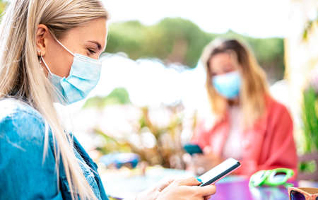 Young woman checking contact tracing app on mobile smartphone - New normal lifestyle concept with zoomers sharing content on social media platforms - Bright vivid filter with focus on left girl faceの写真素材