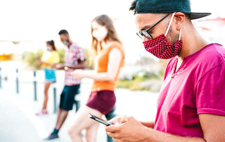Millenial friends wearing disposable face mask using tracking app with mobile phones - Bored young people on smartphones outdoors - New normal lifestyle and social distancing concept - Bright filterの写真素材