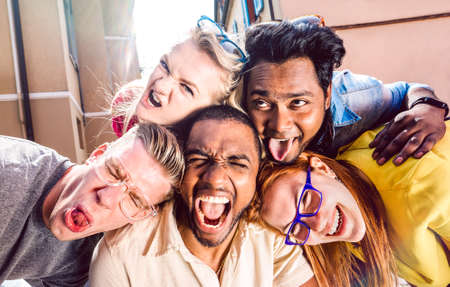Multiracial millenial people taking selfie sticking out tongue with happy faces - Funny life style concept against racism with international young friends having fun together - Warm bright filterの写真素材