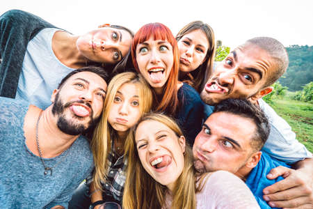 Best friends taking funny selfie at picnic excursion sticking out tongue - Youth life style concept with young people having fun together outdoors - Warm bright filter with focus on central facesの写真素材