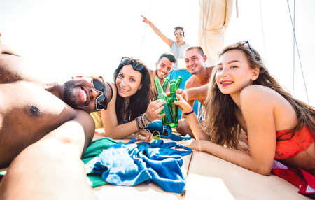 Friends group of guys and girls taking selfie at sailing boat - Luxury life style concept with young multiracial people having fun together at summer beach vacation - Bright vivid sunshine filterの写真素材