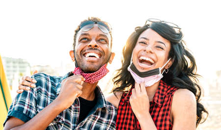 Young couple in love laughing over open face mask - New normal life style and relationship concept with happy lovers on positive mood at beach after lockdown reopening - Warm vivid backlight filterの写真素材