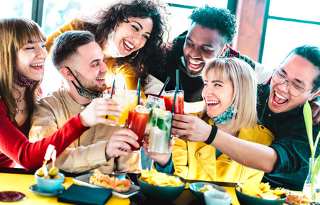 Happy multiracial friends toasting drinks with open face masks - New normal life style concept with youngfriends having fun together after lockdown reopening - Vivid filter with focus on left guyの写真素材
