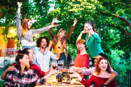 Friends having fun outdoor toasting red wine at garden party - Happy people eating and drinking together in farmhouse winery at night - Friendship concept on warm vivid filterの写真素材
