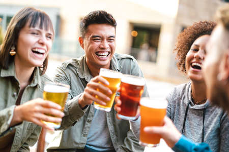 Group of happy multiethnic friends drinking and toasting beer at brewery bar restaurant - Beverage concept with men and women having fun together outsideの写真素材