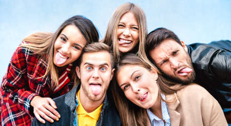 Multicultural milenial guys and girls taking selfie sticking out tongue with happy faces - Crazy life style concept with young students friends having fun together outdoors - Bright vivid filterの写真素材