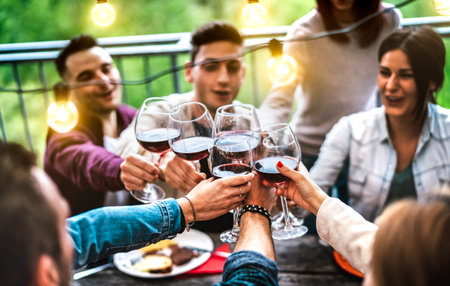 People having fun at farm house after sunset - Happy friends toasting red wine at restaurant under...