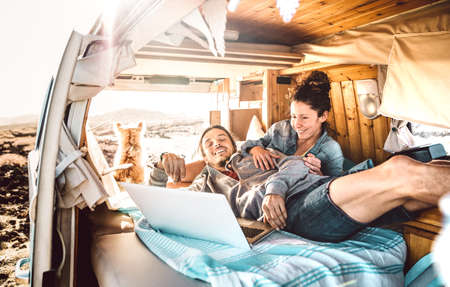 Digital nomad couple traveling together with dog on retro van transport - Freedom life style concept with indie people on minivan adventure sharing content using notebook - Warm backlight filterの写真素材