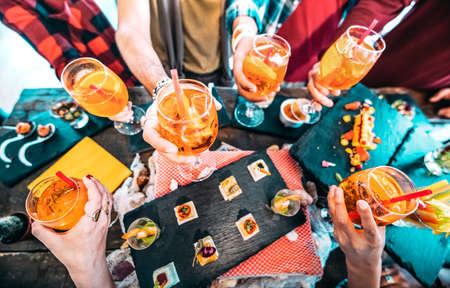People hands toasting multicolored spritz drinks - Trendy friends having fun together drinking cocktails on happy hour at bar buffet - Social gathering party time concept on hipster orange filterの写真素材