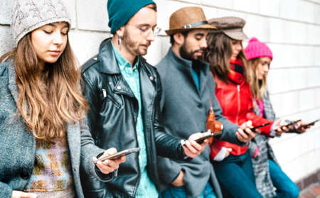 Side view of milenial guys and girls using mobile smartphone - People addicted by smart phone - Life style concept with always connected teenagers - Vivid filter with focus on first left cellphoneの写真素材