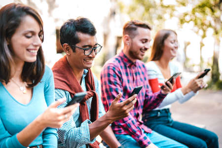 Multicultural students laughing using smartphone at university college campus - Young people friends addicted by mobile smart phone - Technology concept with always connected milenials - Bright filterの写真素材