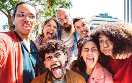 Multi cultural guys and girls taking funny selfie outdoor - Happy milenial life style concept by young multiracial friends having fun day together - Bright warm backlight filter - Focus on lower facesの写真素材