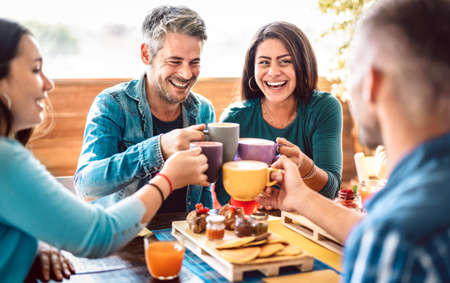 People group toasting latte at coffee bar rooftop - Friends talking and having fun together at cappuccino restaurant - Life style concept with happy men and women at cafe terrace - Bright warm filterの写真素材