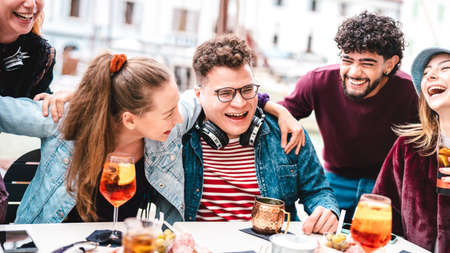 Young friends on genuine laugh moment at fancy pub restaurant - Life style concept with multicultural people having fun together on happy hour at sidewalk cafe - Vivid filter with focus on central guyの写真素材