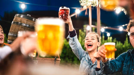 Happy woman clinking and toasting beer at brewery bar restaurant patio with friends - Life style and beverage concept with young people having fun together out side - Focus on face between glassesの写真素材