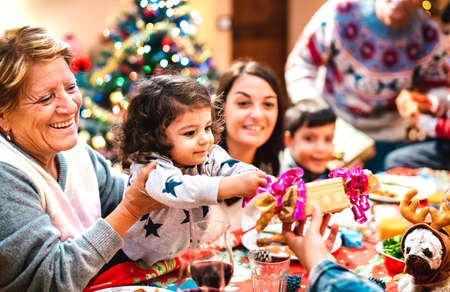 Large multi generation family having fun at christmas home supper - Winter holiday x mas concept with parents and children opening gifts together at dinner - Focus on little daugther - Warm filterの写真素材