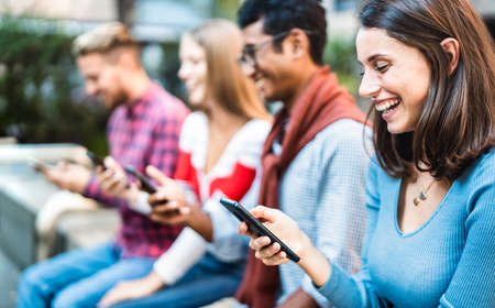 Multicultural group using smartphone at urban city context - Milenial friends addicted by mobile smart phones - Technology concept with always connected millennials with focus on right womanの写真素材