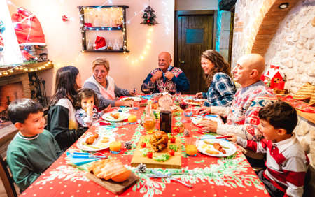 Large multi generation family having fun at holidays dinner event - Winter x mas concept about grand parents eating together with children at home supper feast - Focus on grandfather in the middleの写真素材