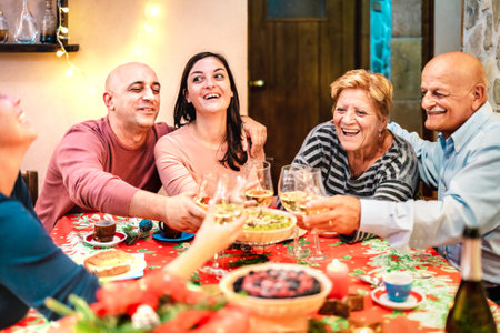 Mixed age group toasting white wine and having fun at winter holiday reunion - Dinner celebration concept with happy adult friends sharing time together at home party - Warm filter with focus on facesの写真素材