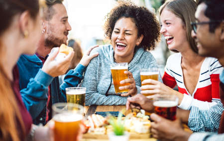 Multiracial friends drinking beer at brewery pub garden - Genuine friendship life style concept with guys and girls enjoying happy hour food together at open air bar dehor - Warm vivid filterの写真素材