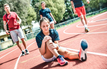 Female sportler getting injured at athletic workout training - Male coach taking care on sport pupil after physical accident - Team concept with young sporty people facing bad mishaps casualtyの写真素材
