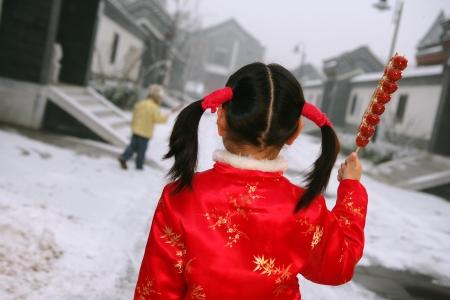 back view of two chinese children holding sugar-coated haws standing in front of a traditonal houseの写真素材