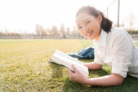 Young female students lying on grass lawn reading book