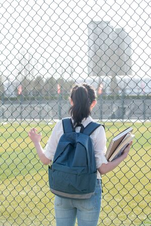back view of Young female students standing outside stadium with holding textbooksの写真素材