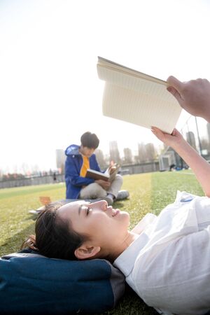 Young college students reading books at campus grass lawnの写真素材
