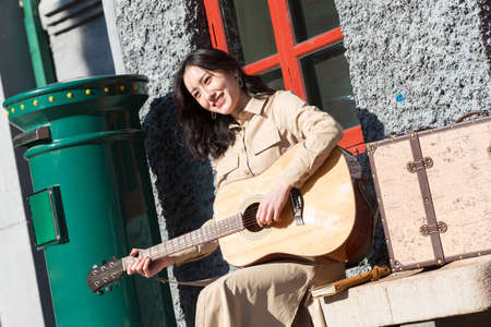 Young woman sitting outside playing the guitar