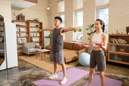 asian young couple exercising with dumbbells in living room at homeの写真素材
