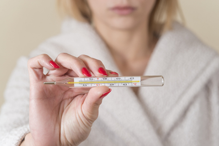 woman holding thermometer in hands, measuring body temperature while suffering from influenza.の写真素材
