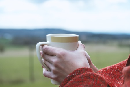 Female holding cup of hot drink in cozy atmosphereの写真素材