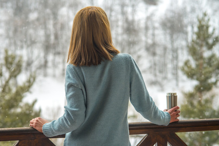 Woman in the background of a winter forest in a thermal bottle in hands