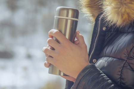 A girl in a winter jacket with a  of coffee or tea in her hand on the balcony in winterの写真素材